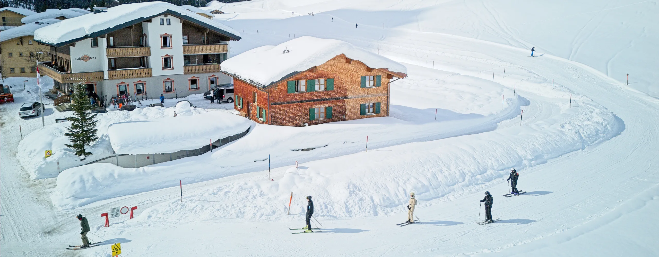 Skifahrer auf einer schneebedeckten Piste neben rustikalen Chalets
