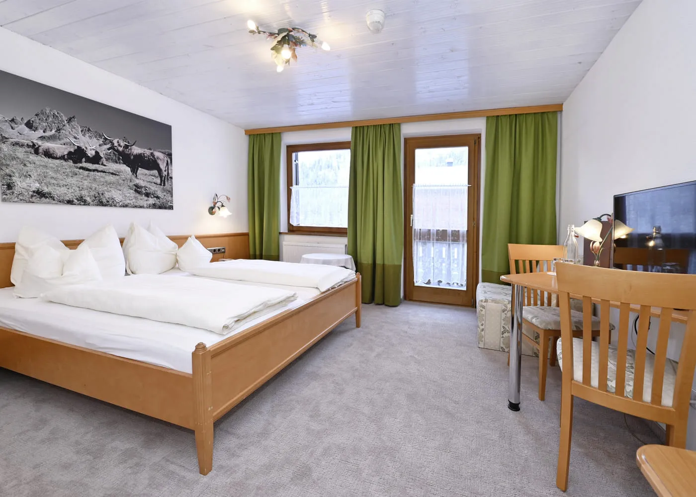 Helles Zimmer mit Doppelbett, Schreibtisch und Zugang zu einem Balkon.