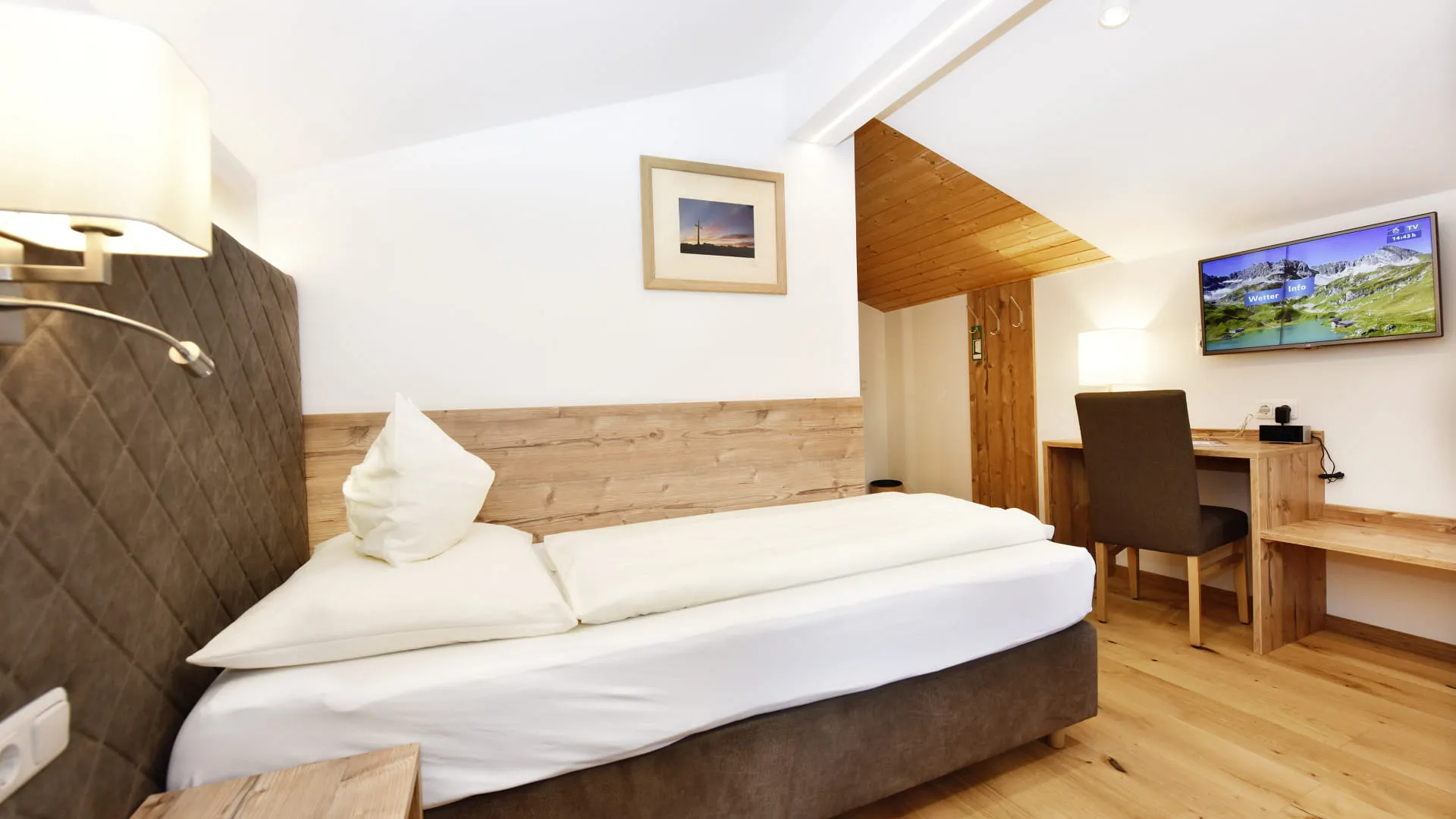 Helles Hotelzimmer mit Doppelbett, Schreibtisch und Fernseher