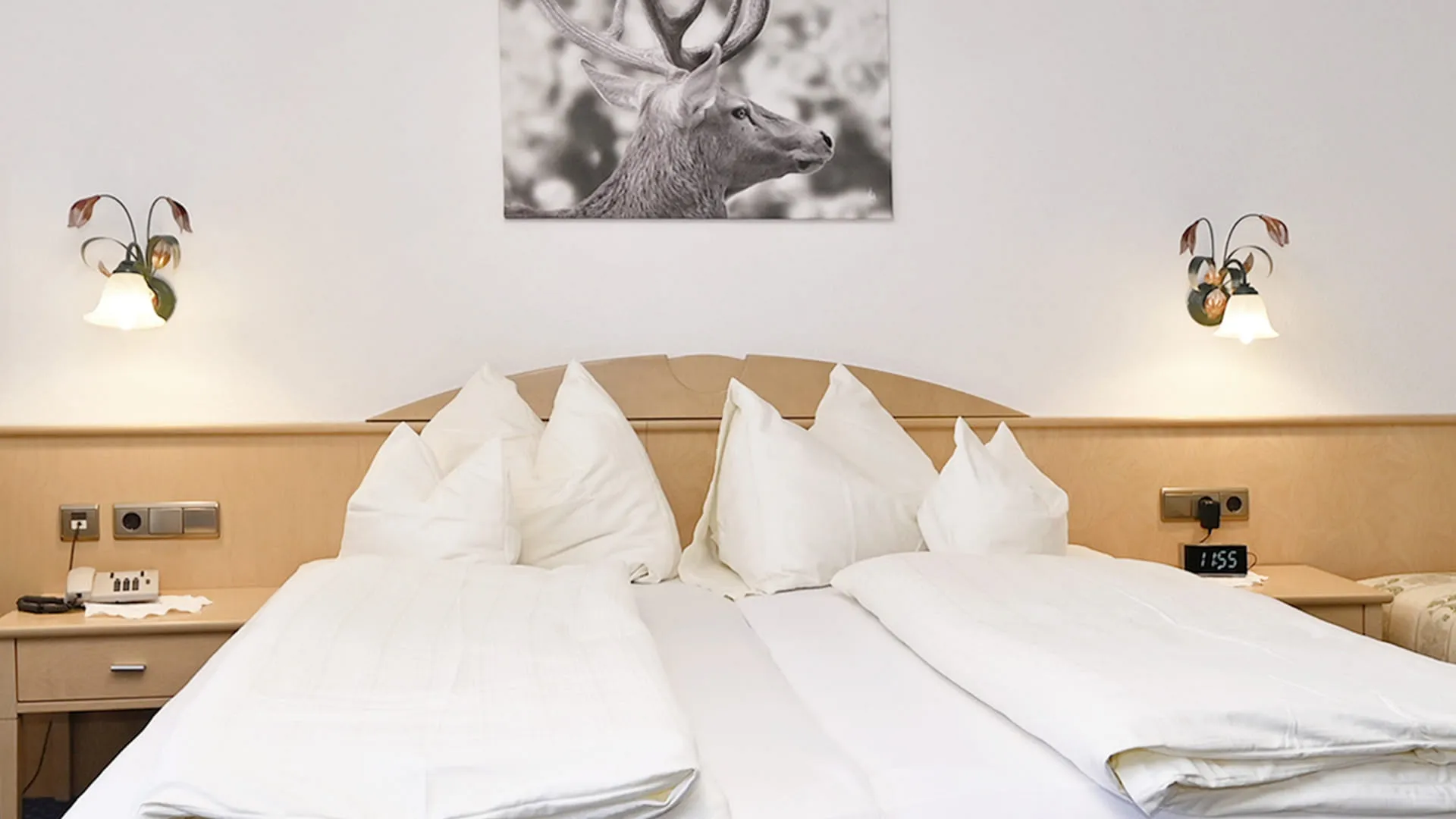 Hotelzimmer mit zwei Betten, weißer Bettwäsche und einem Rehbild an der Wand
