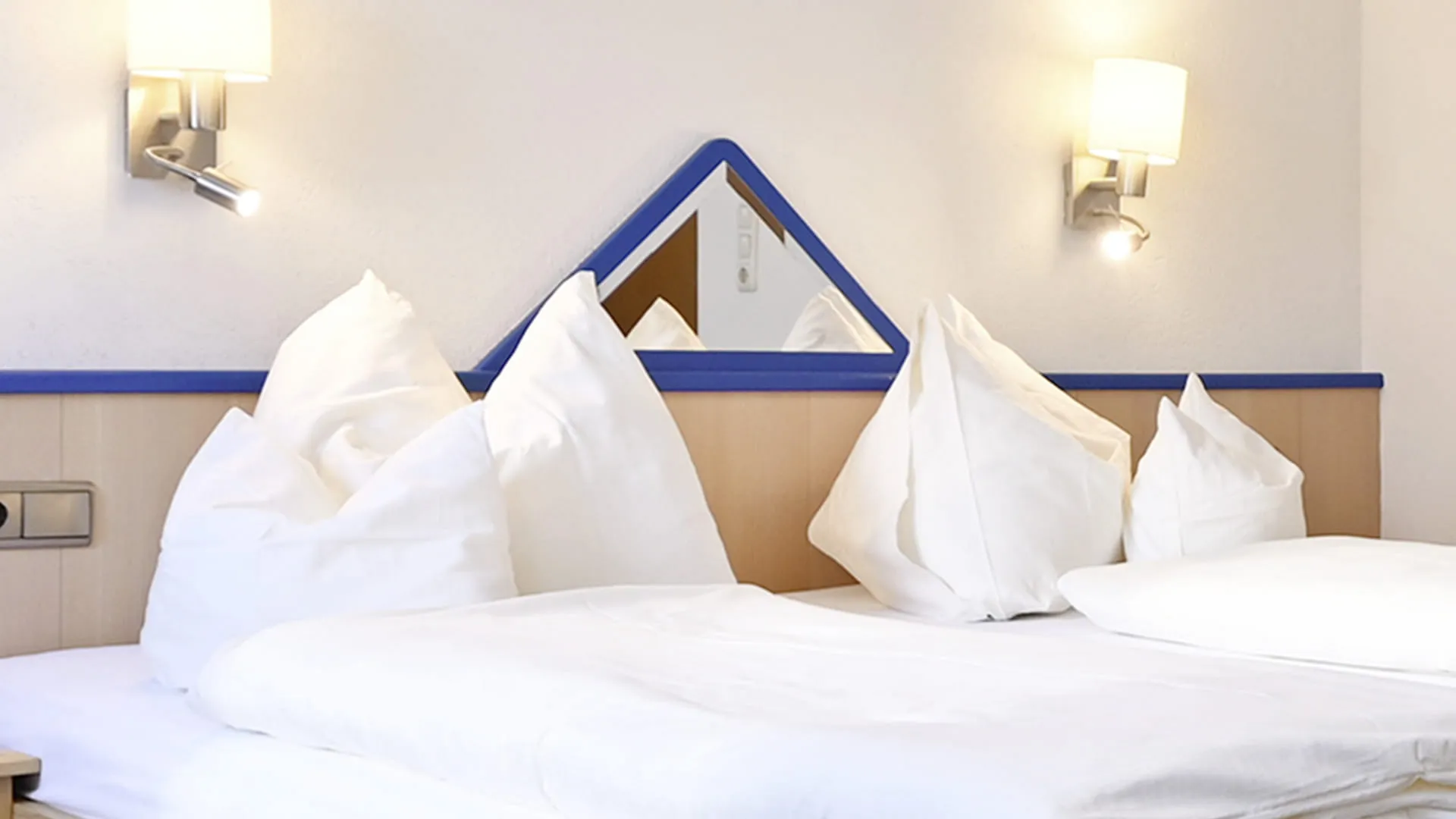 Ein gemütliches Hotelzimmer mit einem Doppelbett, Nachttischlampen und einem dreieckigen Spiegel.