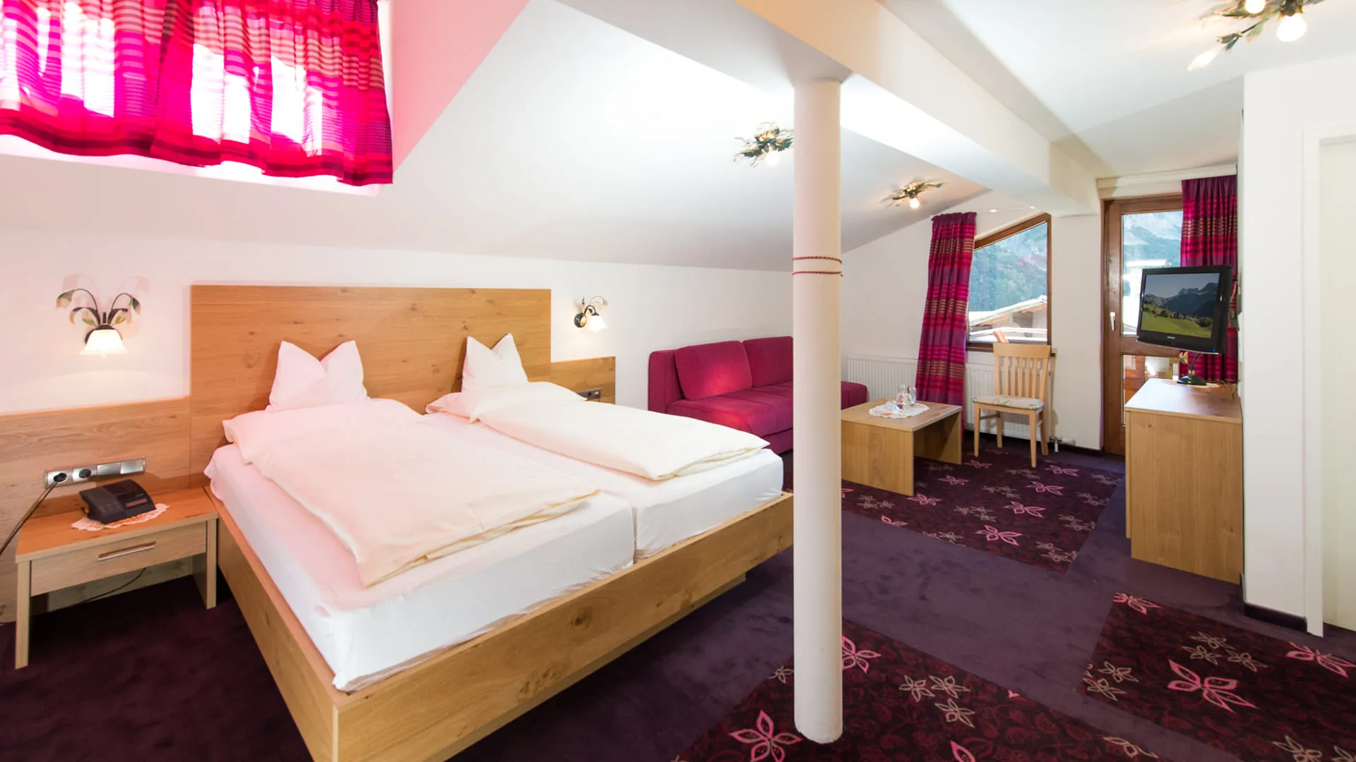 Helles Hotelzimmer mit Doppelbett, Fernseher und roten Vorhängen.