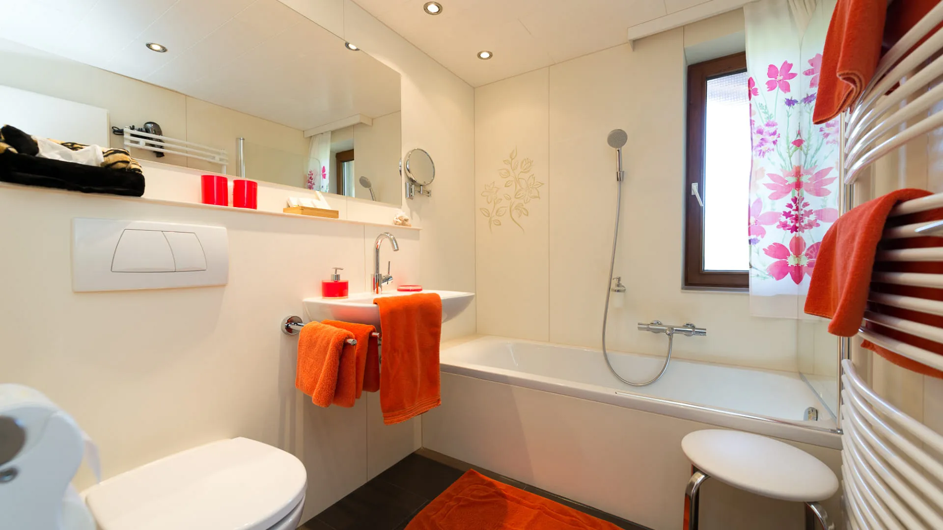 Modernes Badezimmer mit Badewanne, Handtüchern und orangefarbenen Accessoires