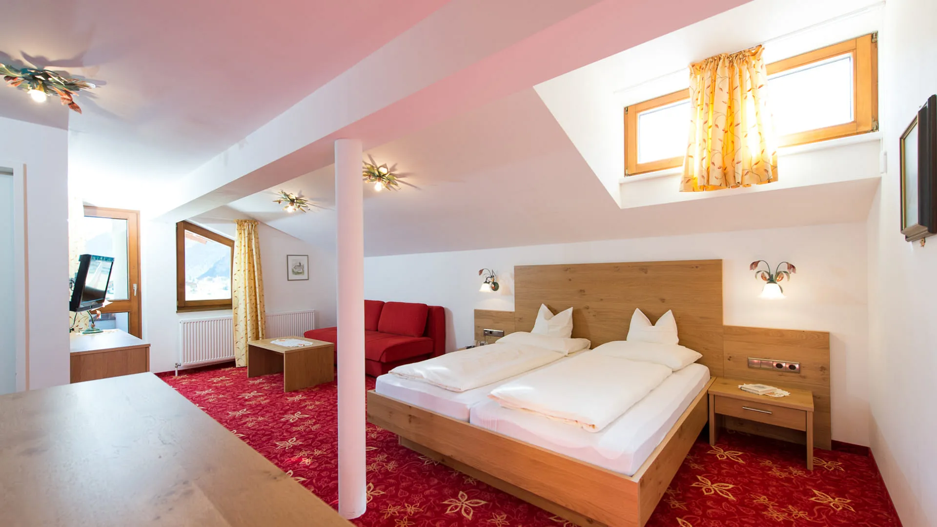 Helles Schlafzimmer mit Doppelbett, rotem Sofa und Fenster.