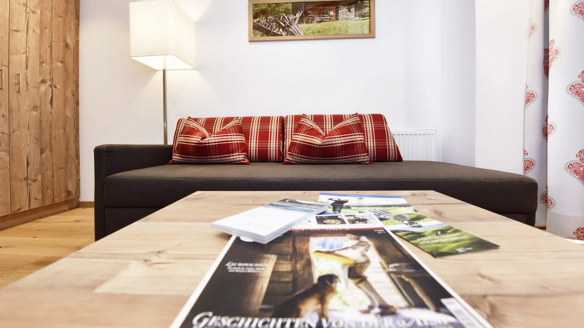 Gemütliches Wohnzimmer mit Sofa, Karokissen, Lampe und Holztisch.