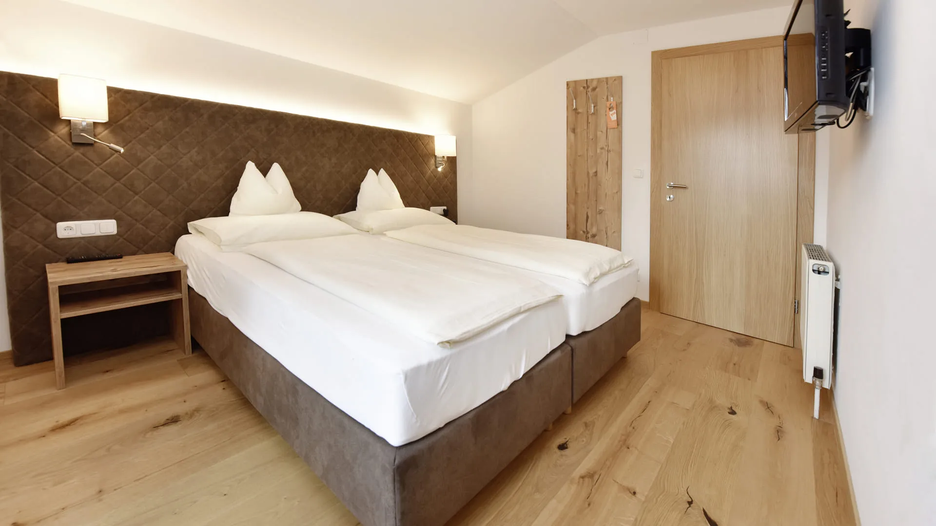 Helles Hotelzimmer mit zwei Einzelbetten, Holzfußboden und TV.