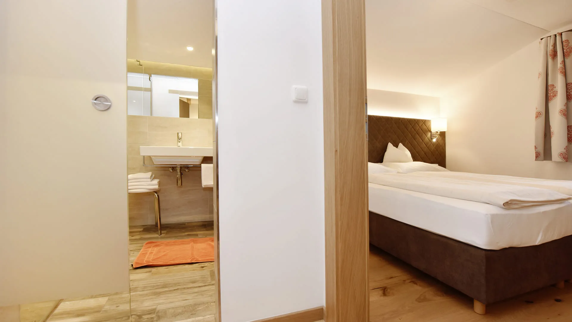 Helles Schlafzimmer mit Badezimmer, Holzfußboden und schöner Beleuchtung.