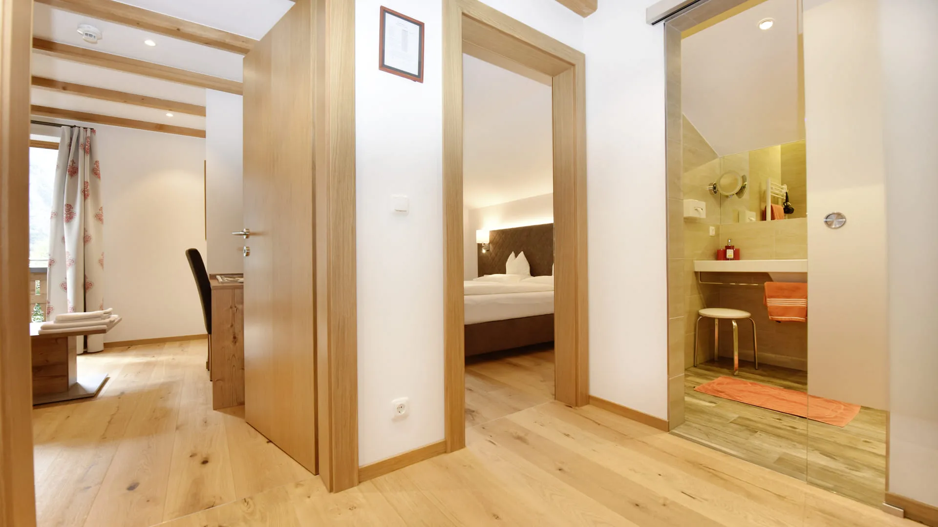 Blick in einen Flur mit Holzboden, Türen zu Wohn- und Badezimmern, Licht und Möbeln.