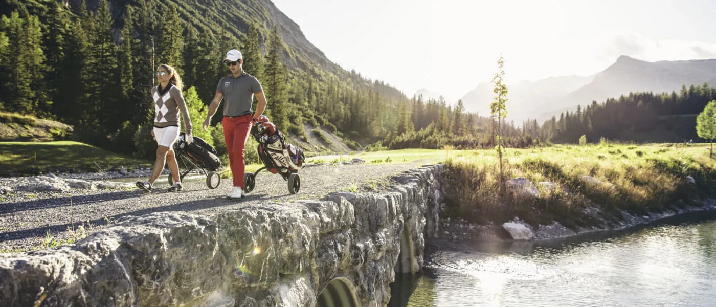 Paar mit Golftaschen spaziert in Lech Zürs.
