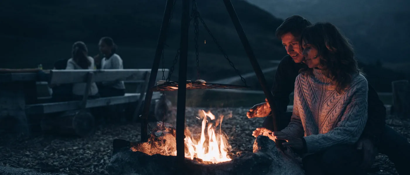 Paar am Lagerfeuer in Lech Zürs, entspannte Abendatmosphäre.