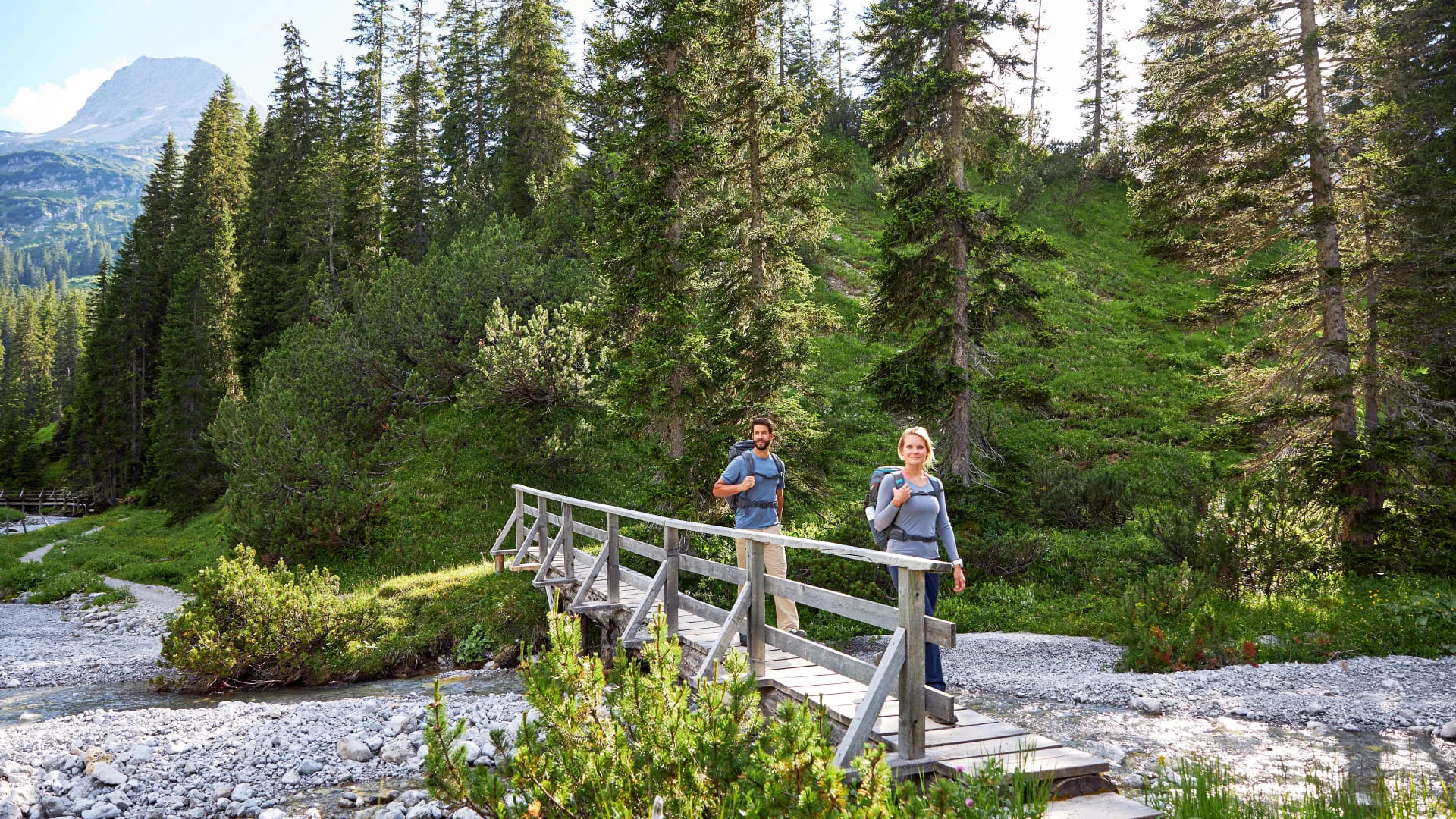 Paar auf einer Brücke in einem Waldgebiet, umgeben von Bergen