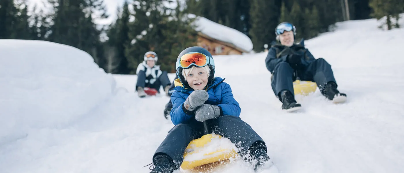 Kinder und Erwachsene fahren mit Zipfelbobs im Schnee von Lech Zürs.