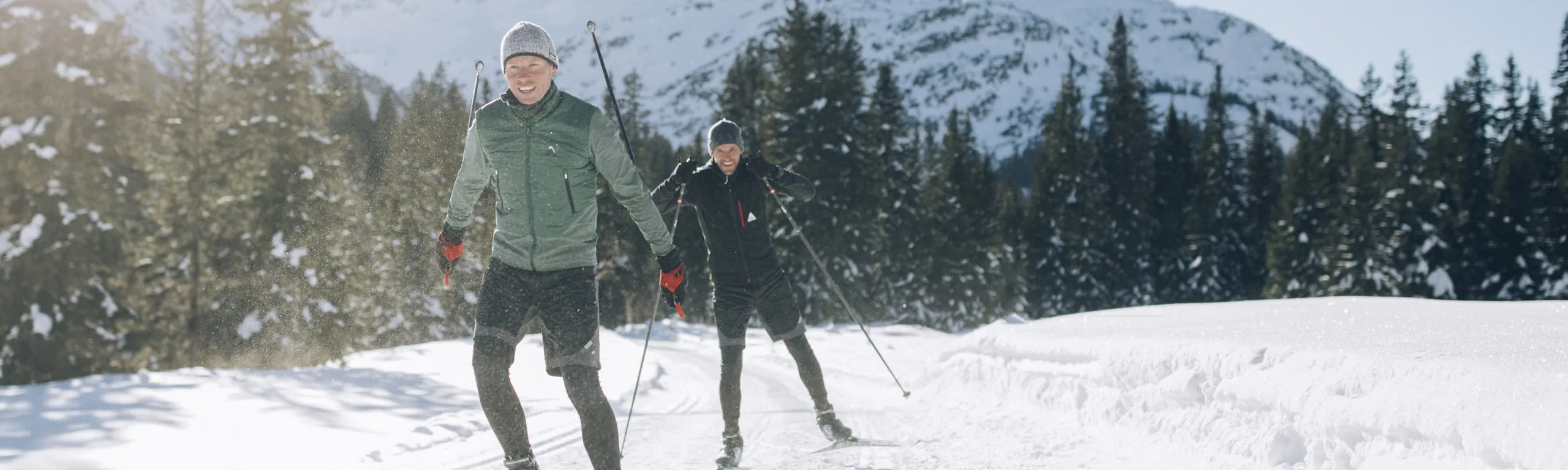 Zwei Langläufer im Schnee mit verschneiten Bergen im Hintergrund