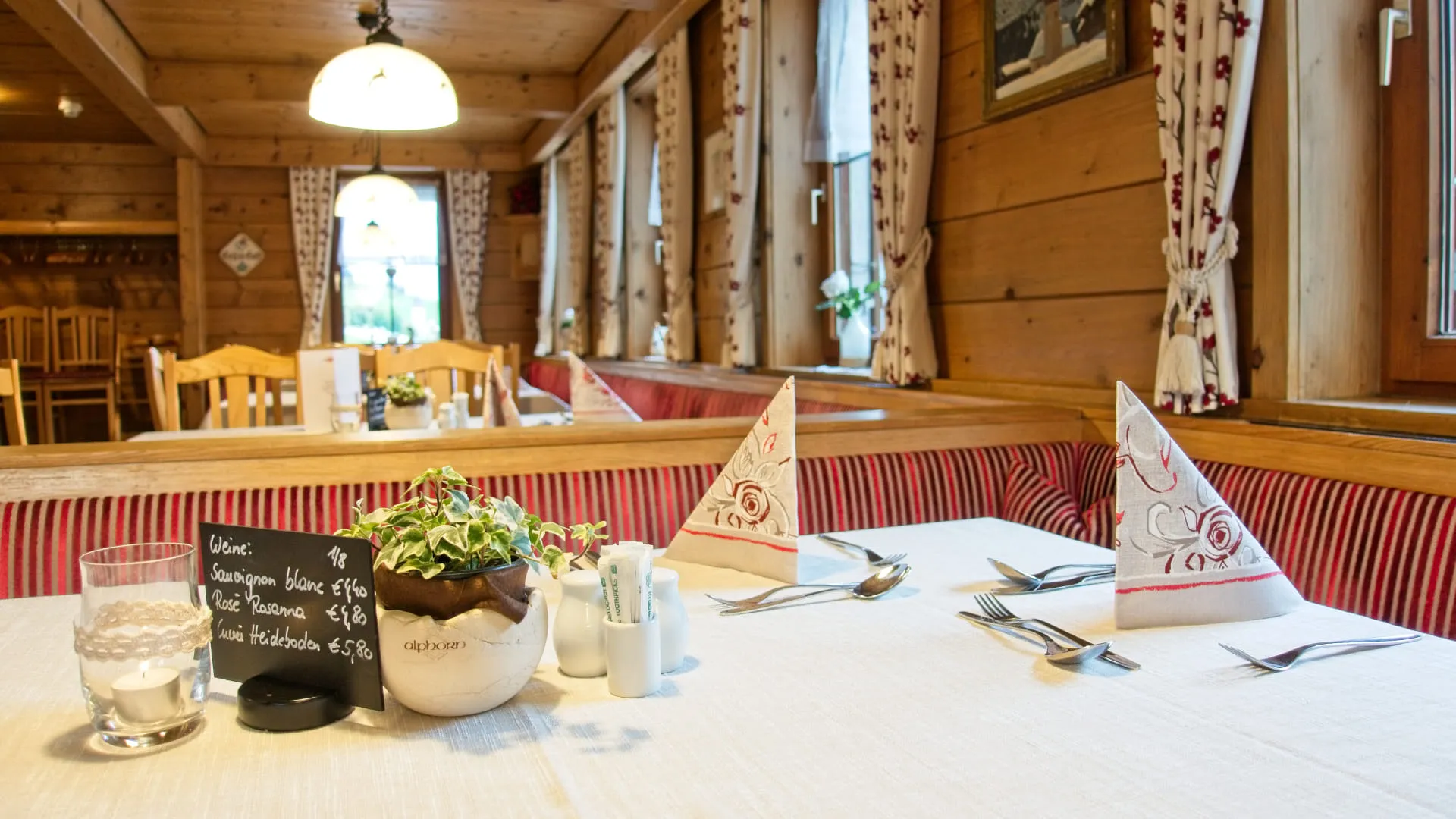 Gemütlicher Gastraum mit Tischgedeck, Blumen und dekorierten Servietten.